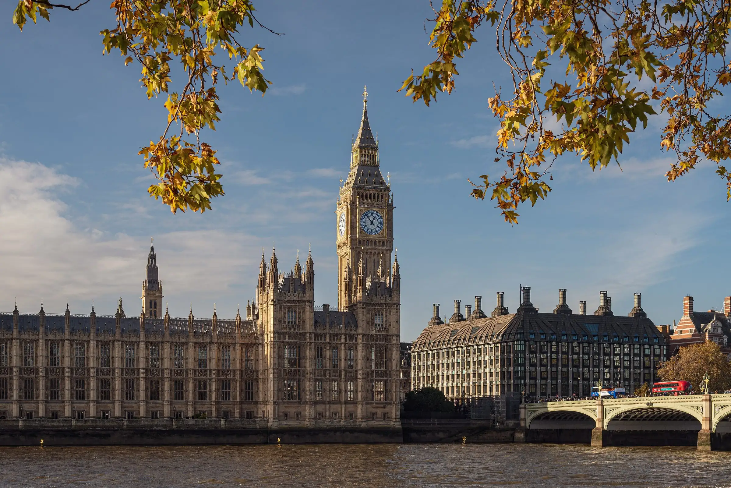 The Houses of Parliament and Big Ben across the Thames under autumn leaves