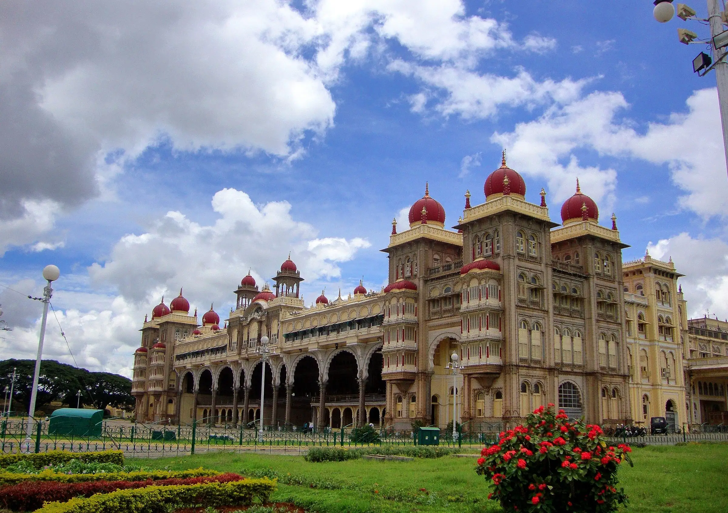Mysore Palace under a blue sky with red domes and a garden in front