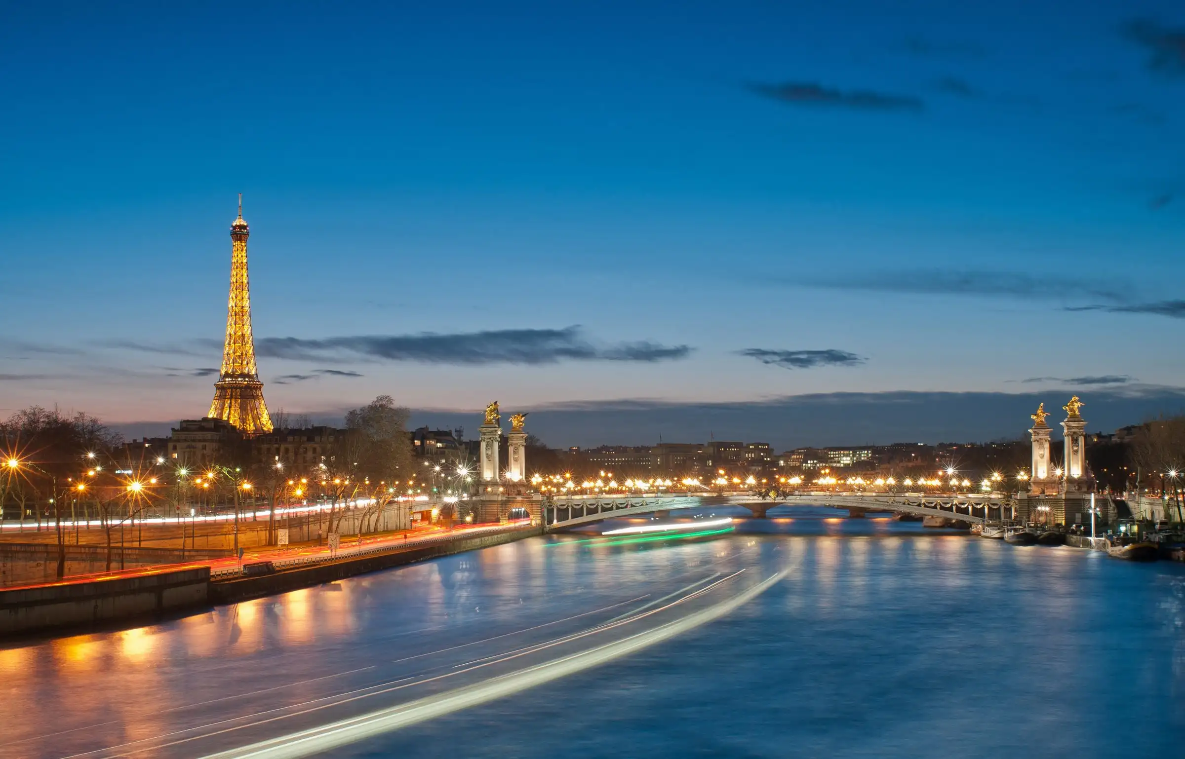The Eiffel Tower and the Seine at dusk with light trails from boats
