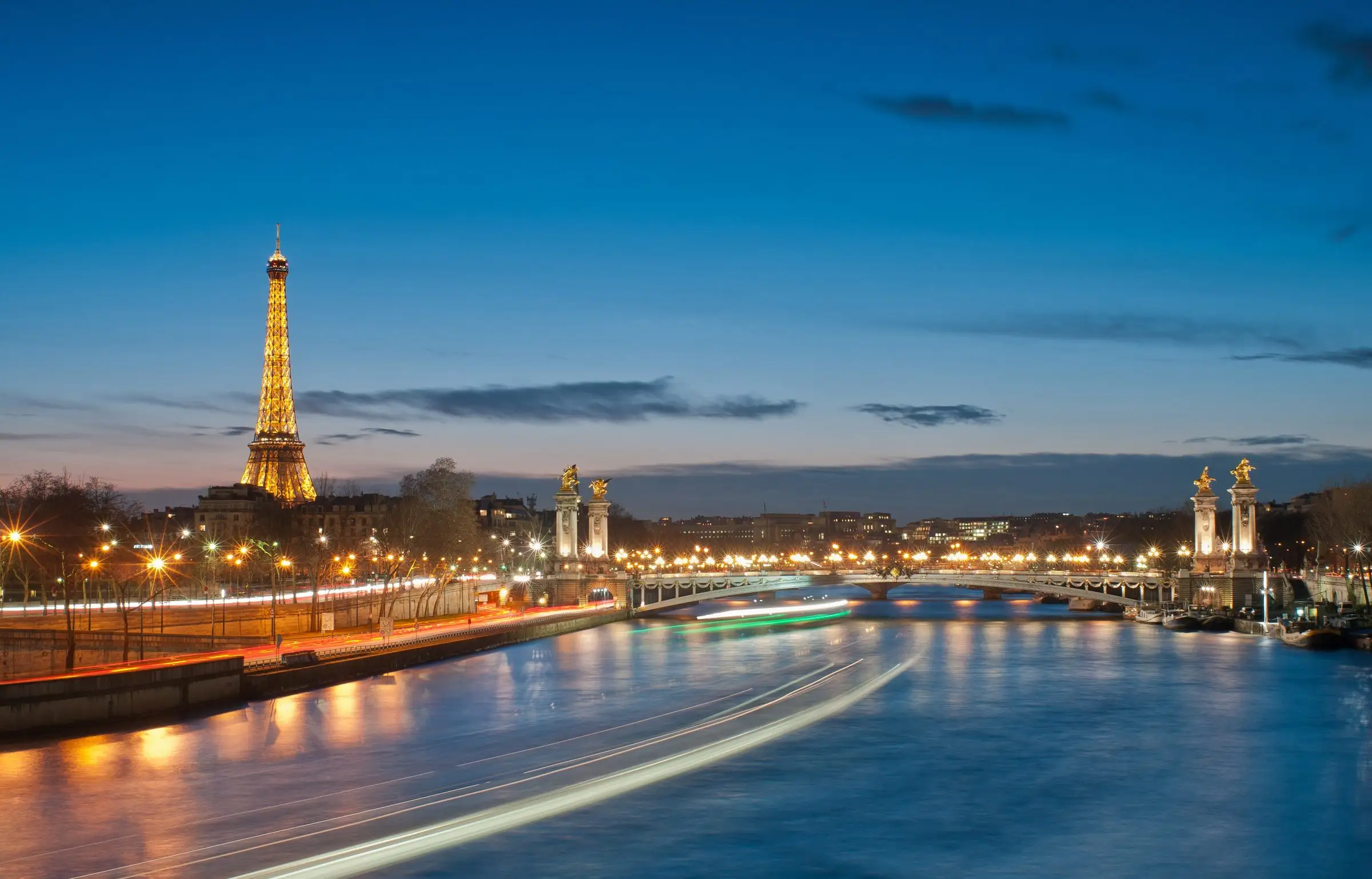 The Eiffel Tower and the Seine at dusk with light trails from boats