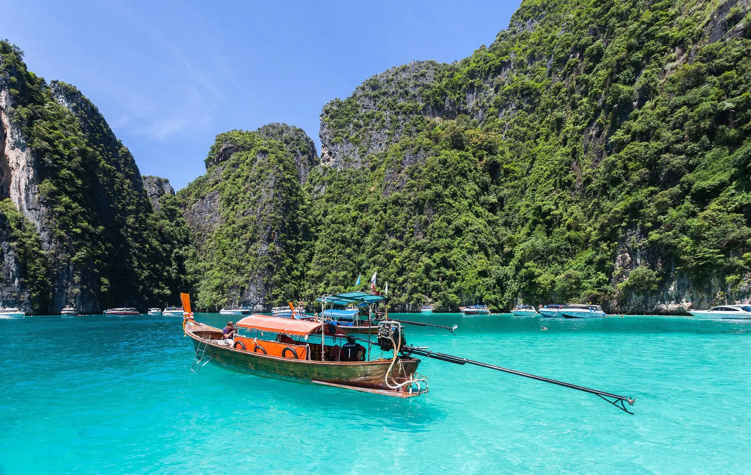 A longtail boat on turquoise water below green limestone cliffs at Phi Phi